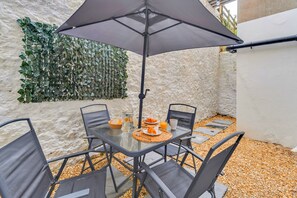 Mesa de vidrio con sillas, una sombrilla y una pared cubierta de follaje verde.