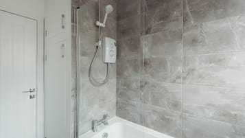 A modern bathroom with a bathtub, a shower with a handheld showerhead, and a control panel.
