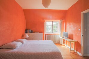 Et soveværelse med seng, skrivebord med fjernsyn, radiator og et vindue med gardiner.