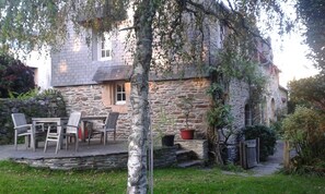 En bygning i sten med en patio, udendørs siddepladser og plantekasser.