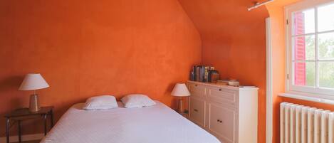 Un dormitorio con cama, dos lámparas de noche, una mesita de noche, un aparador y una ventana con contraventanas.