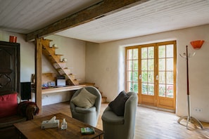 A room with a wooden staircase, a sofa, a table with a tissue box and book, and a window with a view of greenery.