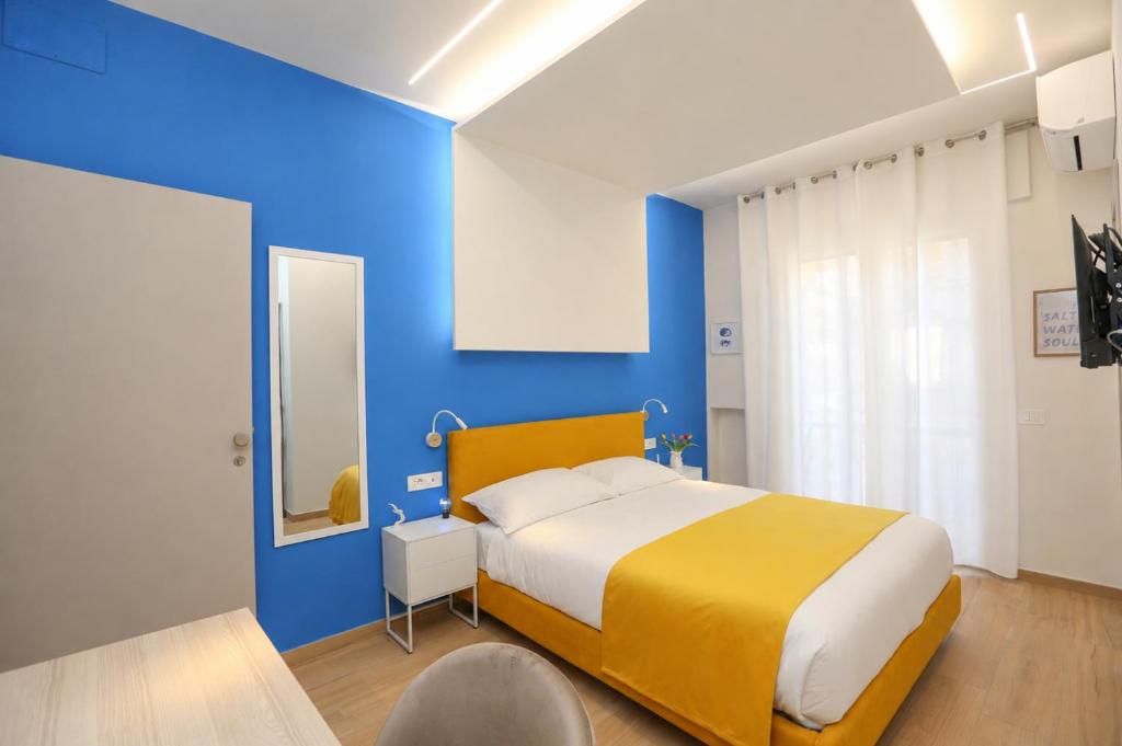 A hotel room with a bed, a bedside table, a mirror, and a window with curtains.