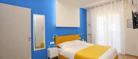 A hotel room with a bed, a bedside table, a mirror, and a window with curtains.