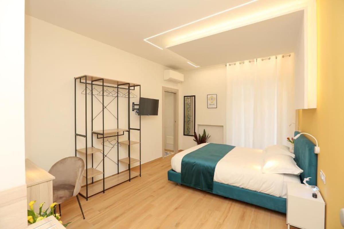 A modern bedroom with a bed, a desk, a chair, and a walk-in closet.