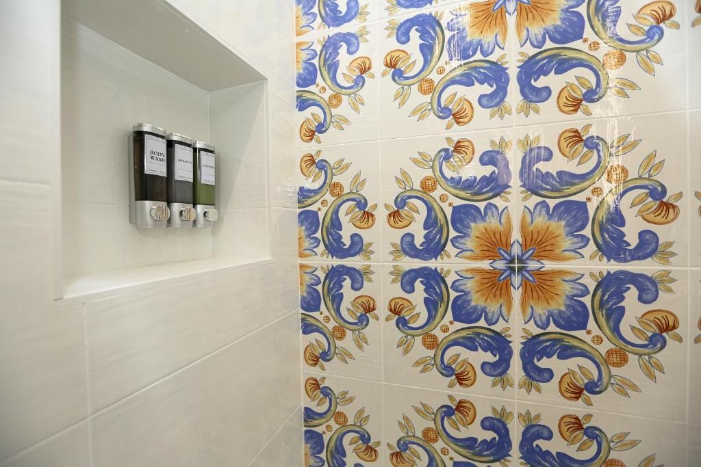 Baño con pared de azulejos con diseño floral y repisas con dispensadores de jabón de cuerpo.