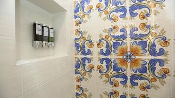 Baño con pared de azulejos con diseño floral y repisas con dispensadores de jabón de cuerpo.