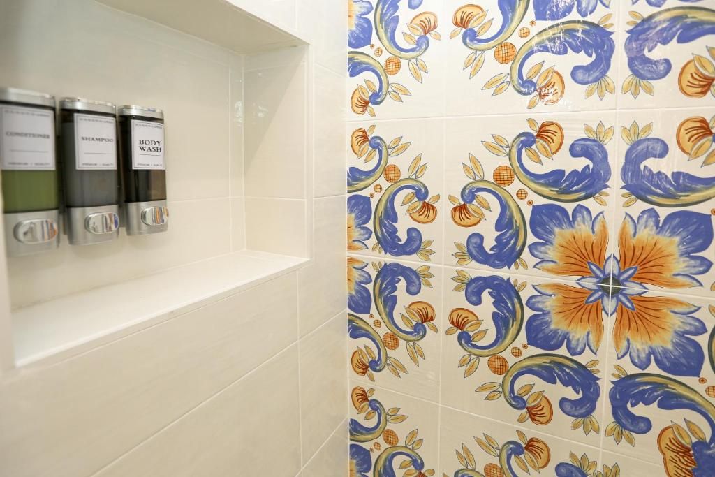 Ein Badezimmer mit einer gefliesten Wand, die ein Blumenmuster zeigt, und drei Spendern mit den Aufschriften 'shampoo', 'shampoo' und 'body wash'.