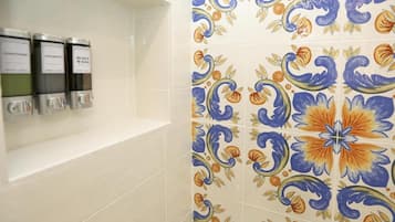 Ein Badezimmer mit einer gefliesten Wand, die ein Blumenmuster zeigt, und drei Spendern mit den Aufschriften 'shampoo', 'shampoo' und 'body wash'.