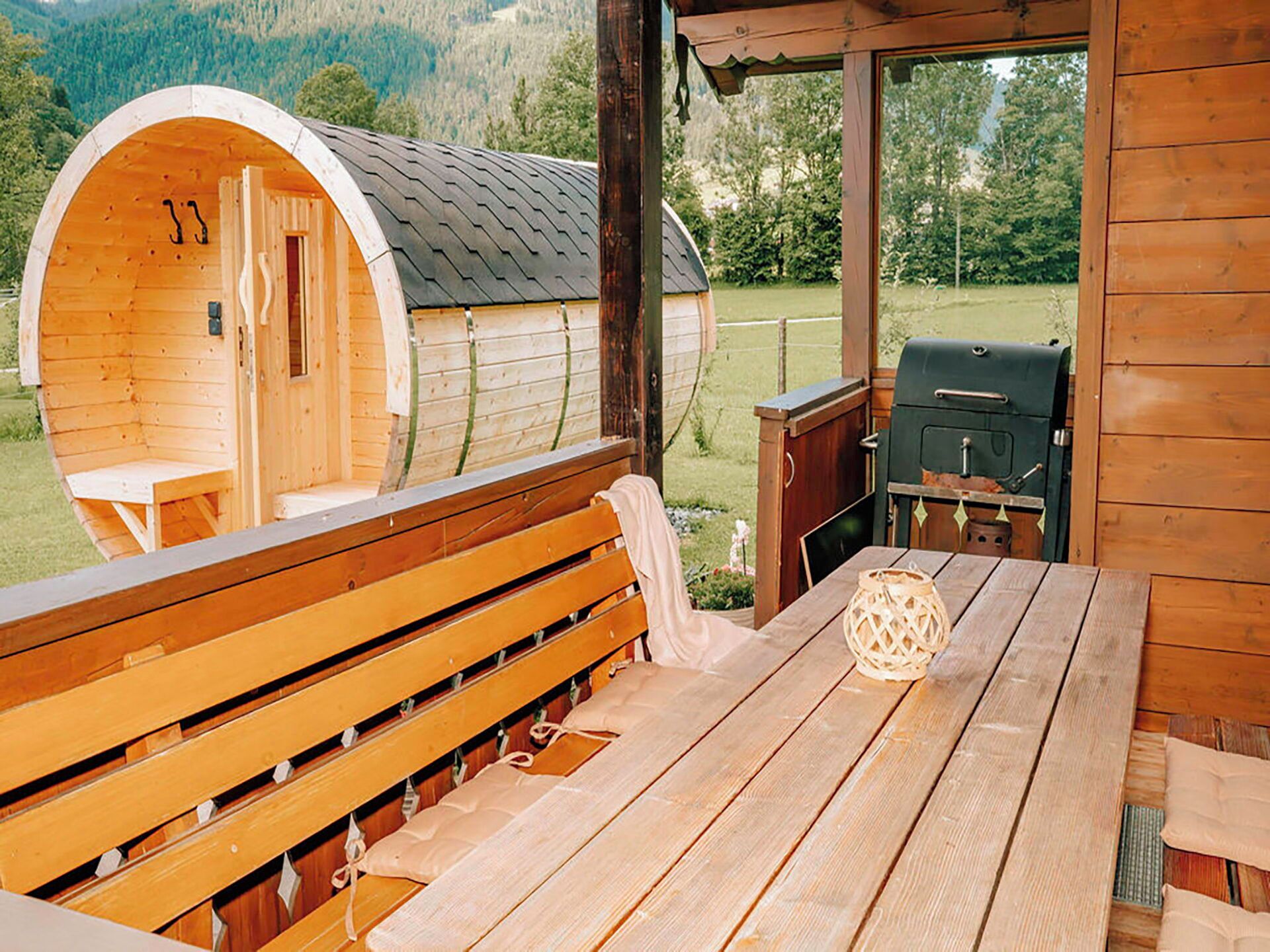 A wooden cabin with a curved sleeping area, a bench, a table, and a grill outside.