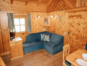 Ein gemütliches Blockhauskamin-Interieur mit einer Eckcouch, Holzwänden, einem Esstisch und einem Fenster mit Vorhängen.