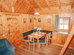 Ein Holzinterieur mit Esstisch, Stühlen, einer Bank und einem Fenster mit Vorhängen.