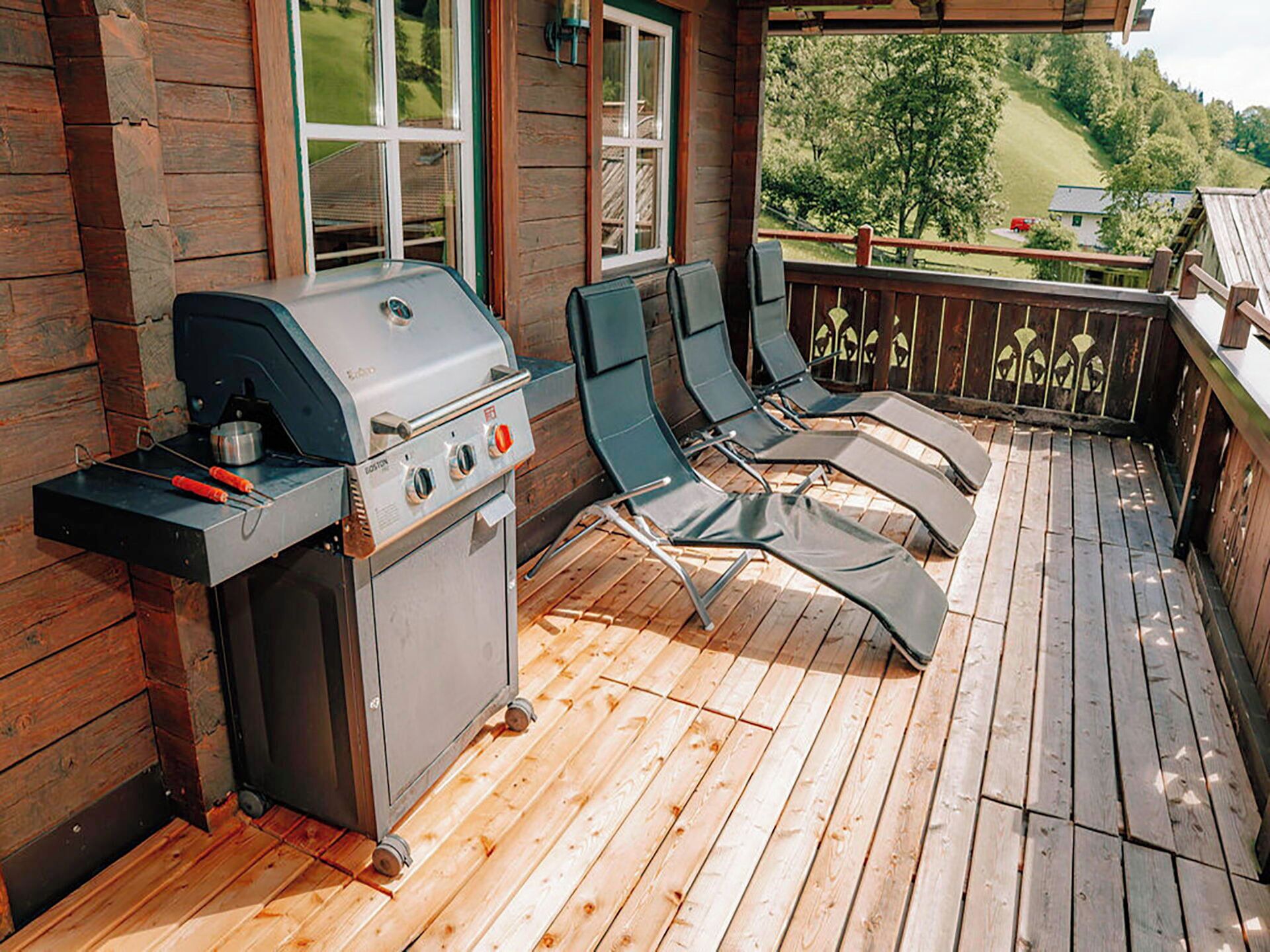 Een terras buiten met een barbecue en lounge stoelen.