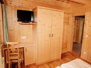 Ein Zimmer aus Holz mit einem Bett, einem Schreibtisch, einem Kleiderschrank und einem Fernseher.