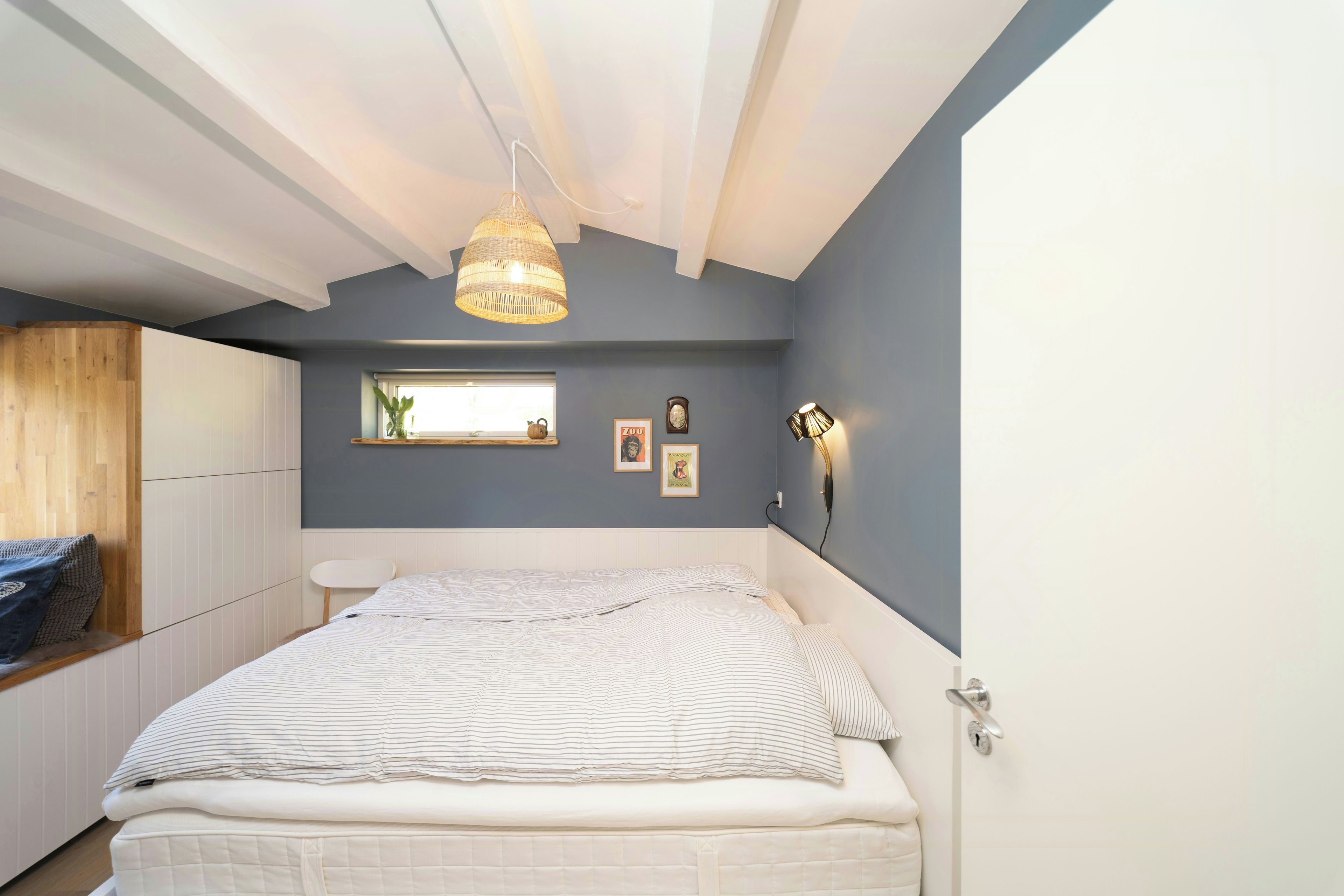 A bedroom with a bed, a window, a wall clock, and a hanging light fixture.
