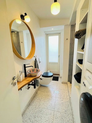 Et badeværelse med et rundt spejl, toilet, vask og hylder.