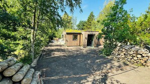 Eine kleine Holzhütte mit grüner Dachdeckung, umgeben von Bäumen und einem Kiesweg, der dorthin führt.