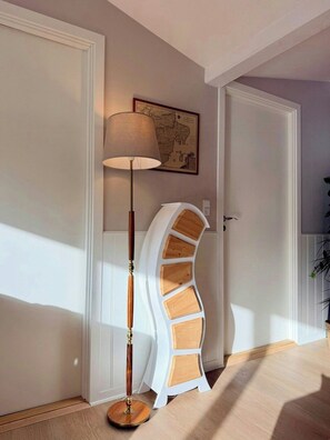Un pasillo con una lámpara de pie, un mapa en la pared y un mueble blanco de diseño curvo.