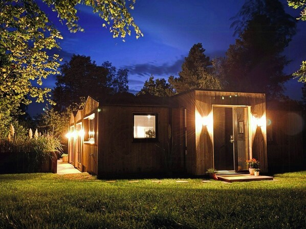 Una cabaña de madera con puerta de vidrio, una ventana pequeña y un porche con plantas en macetas.
