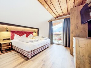 Ein Schlafzimmer mit Holzboden, einem Bett mit kariertem Überwurf, einem Nachttisch und Blick ins Freie durch ein Fenster.