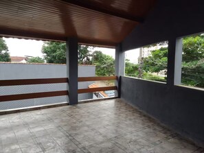 Ein überdachter Balkon mit Blick auf Grünflächen und Gebäude.