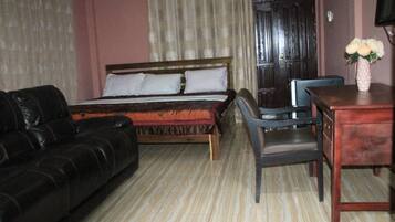 A room with a bed, a black leather sofa, a wooden desk, and a chair.