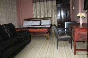 A room with a bed, a black leather sofa, a wooden desk, and a chair. - Sika Towers Hotel limited (Ahenema Kokobin)