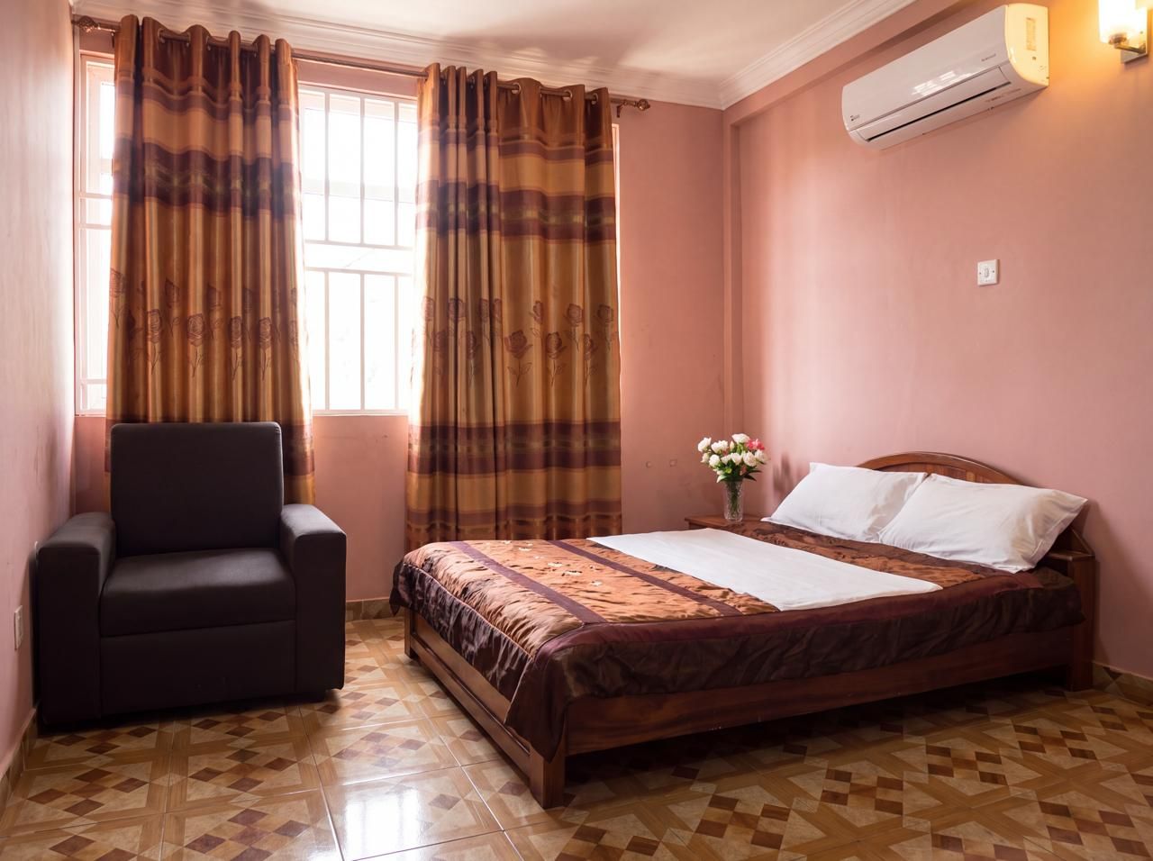 A bedroom with a bed, a chair, a window with curtains, and an air conditioning unit.