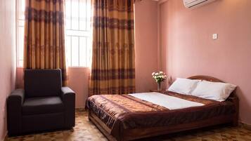 A bedroom with a bed, a chair, a window with curtains, and an air conditioning unit.