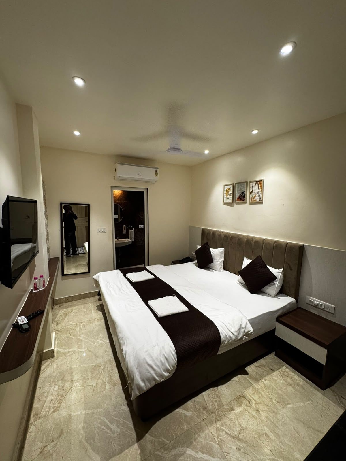 Habitación de hotel con una cama grande, mesitas de noche, televisor y aire acondicionado.