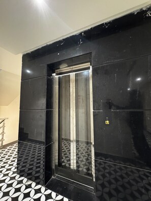 A black elevator with a metallic interior, surrounded by black walls and a patterned floor. - Hotel Skyrooms Inn (Varanasi)