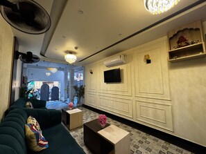 A hotel lobby with a sofa, a coffee table, a TV, and a chandelier. - Hotel Skyrooms Inn (Varanasi)