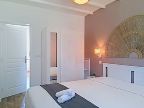 Ein Hotelzimmer mit Bett, Schrank, Nachttisch mit Lampe und einem großen dekorativen Spiegel an der Wand.