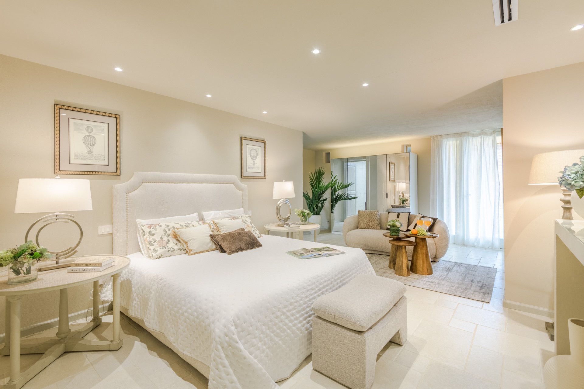 A hotel bedroom with a large bed, bedside tables, a sitting area with a sofa, and a dining table.