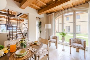 A dining area with a wooden table set for a meal, a staircase, and large windows with a view of a building and greenery outside. - Villa Altavista in Montecarlo (Montecarlo)