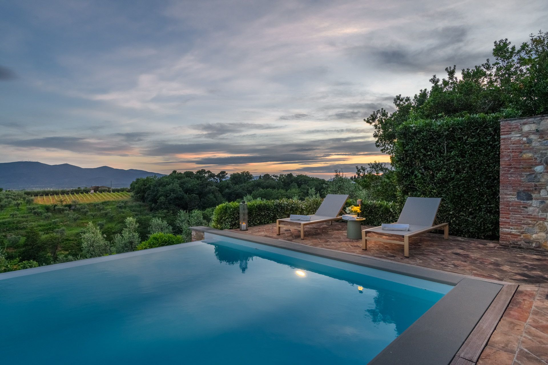 A swimming pool with two lounge chairs and a brick wall.