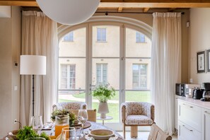 A dining area with a table set for two, a potted plant, and a view of a building through large windows. - Villa Altavista in Montecarlo (Montecarlo)