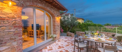 A stone building with a patio area featuring a table set for dining, surrounded by chairs.