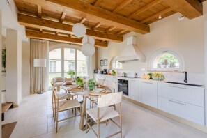 Cozinha moderna com armários brancos, área de jantar com mesa redonda e cadeiras, e uma janela grande que oferece luz natural.