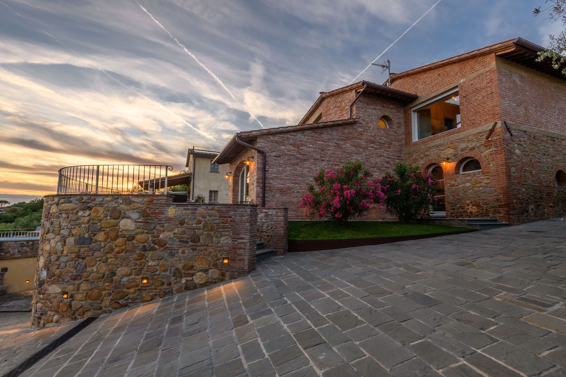 A stone-walled building with a brick facade, a stone staircase, and a well-maintained garden with pink flowers.