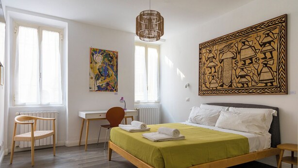 A bedroom with a bed, a desk, a chair, a radiator, and artwork on the walls. - Urbana Otto - Designer home in the heart of Monti (Roma)