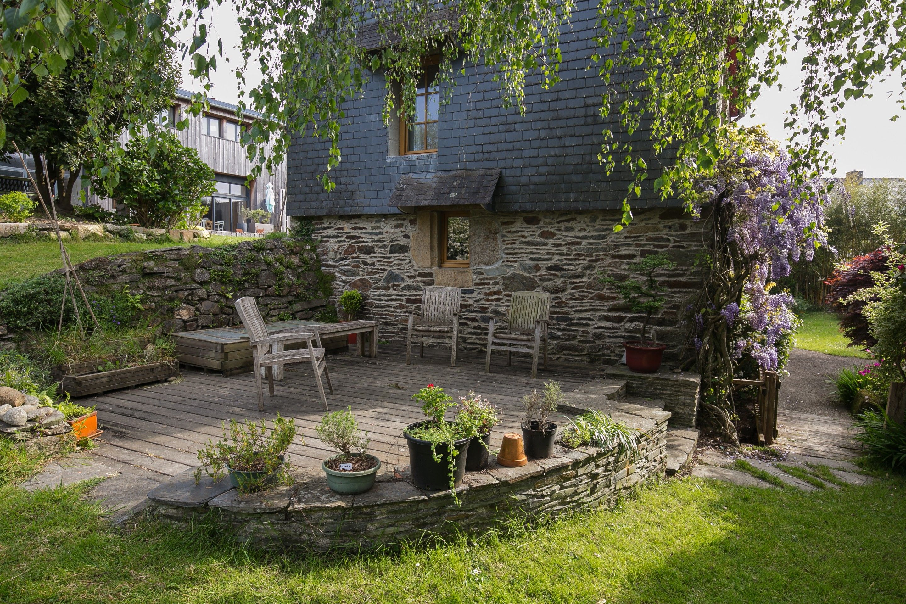 Ein Haus aus Stein mit einer Holzterrasse, Sitzgelegenheiten im Freien und Topfpflanzen.