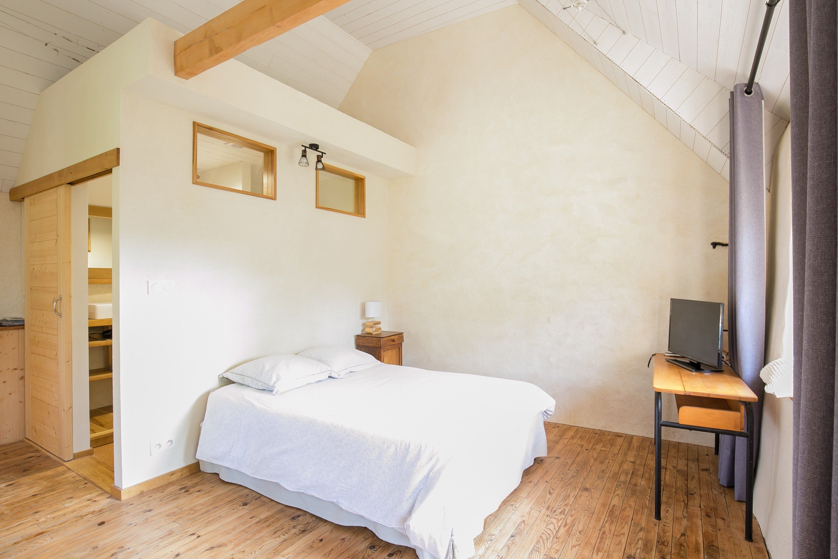 Een slaapkamer met een bed, een bureau met een computer, een nachtkastje en een kledingkast.