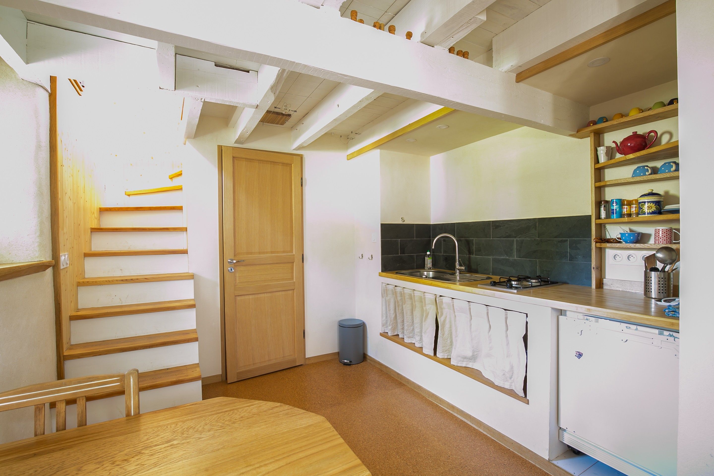 Una cocina con una escalera de madera, un fregadero, una estufa y una repisa con utensilios de cocina.