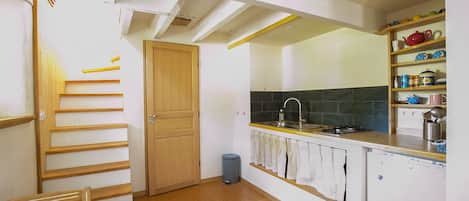 A kitchen with a wooden staircase, a sink, a stove, and a shelf with kitchenware.
