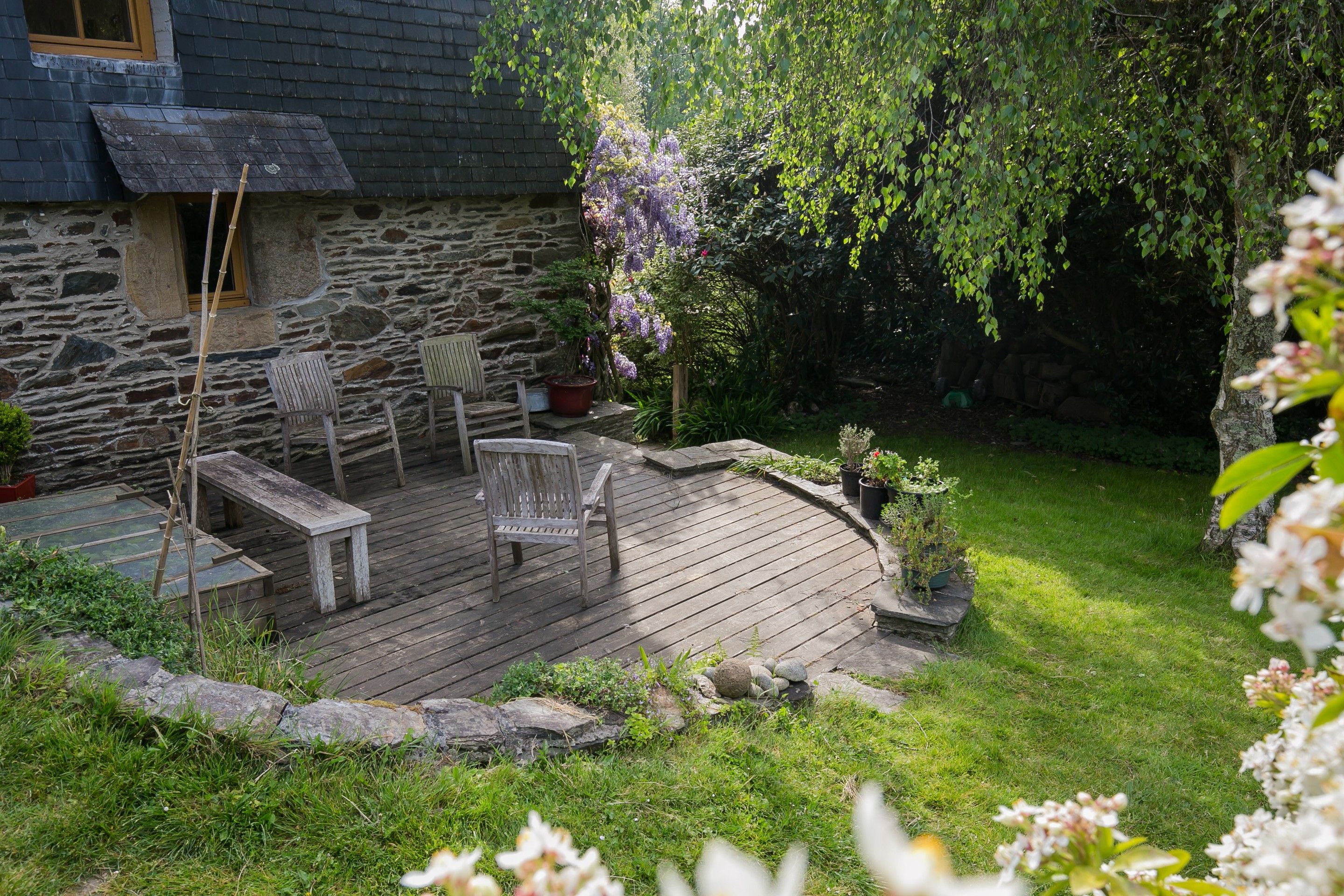 A stone house with a wooden deck, two wooden chairs, and a small table.