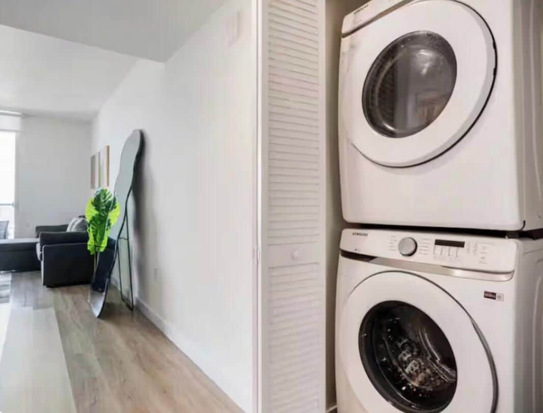 A modern laundry room with stacked washing machines, a potted plant, and a minimalist design.