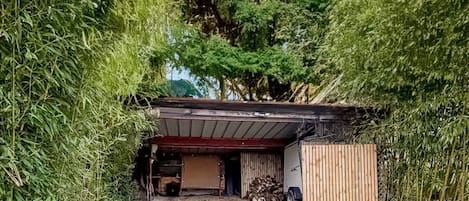A covered outdoor area with a wooden structure, a vehicle, and a pile of firewood.
