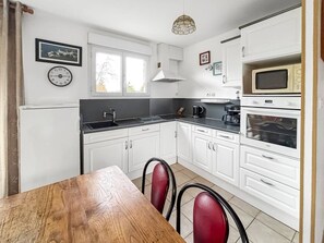 A kitchen with white cabinets, a wooden table, and red chairs. - Cozy house with a large garden (Saint-Avé)