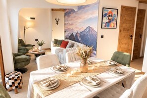A dining area with a long table set for four, a vase with flowers, and a mountain landscape mural on the wall. - L'Ultime 1800 - Avoriaz - Sleeps 6 - Premium (Morzine)
